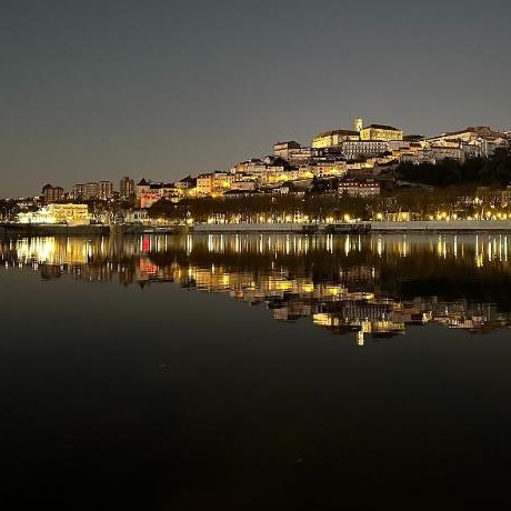 Colina de Coimbra iluminada à noite, refletida no rio